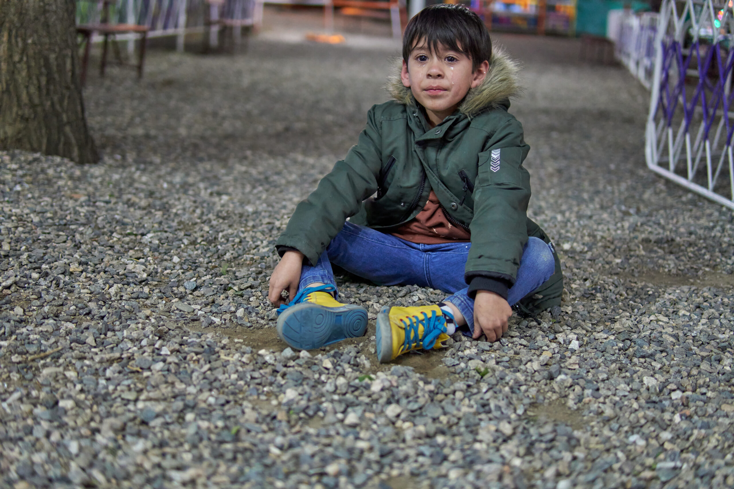 latino boy sitting alone on the ground in an amusement park in anguish with tears streaming down his face